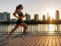 Спорт і рух - Світло і тінь Бігунка на набережній під час сходу сонця, міський пейзаж, світло